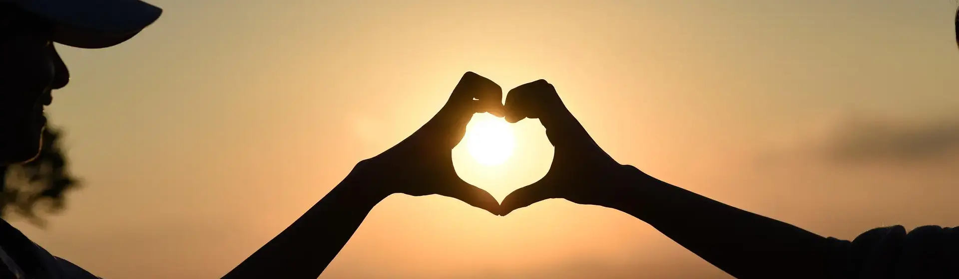 zwei Menschen formen mit ihrer Hand ein Herz, die Sonne scheint hindurch